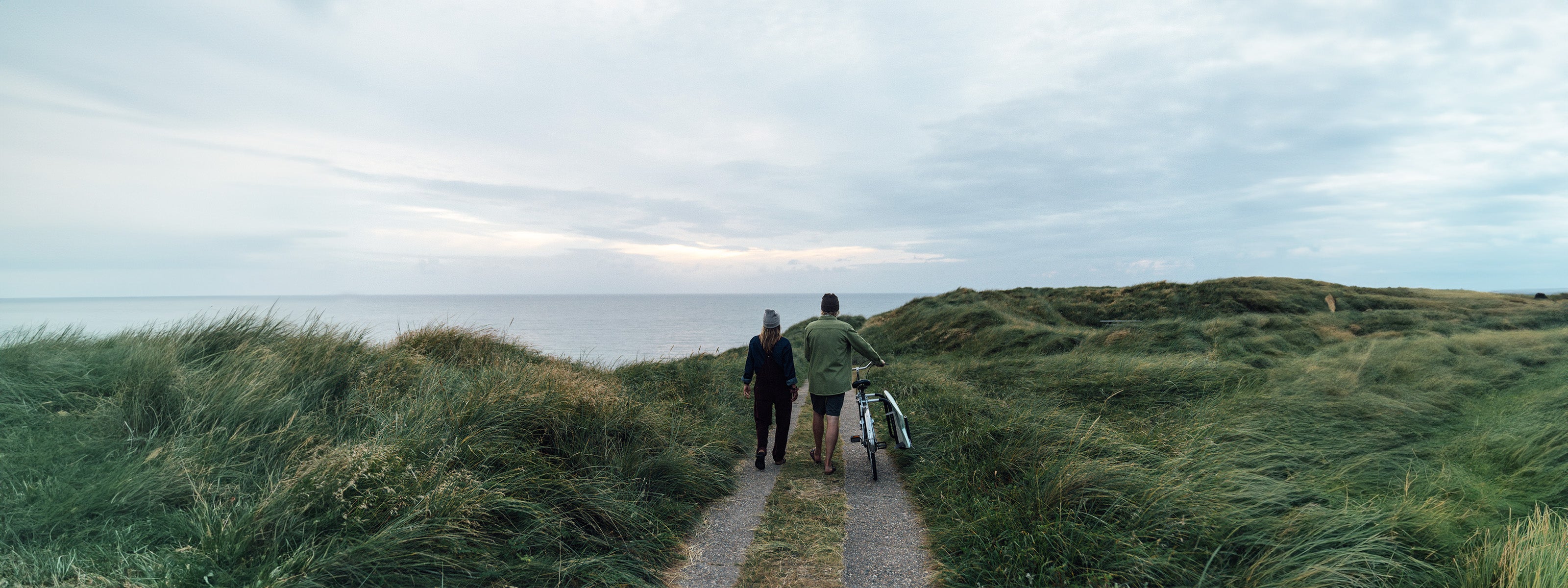 Frau und Mann spazieren auf einem Weg in den Dünen am Meer auf einem Foto von Lakor. 